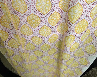 May include: Close-up of a fabric with a repeating pattern of yellow, leaf-shaped designs on a white background. The leaves are outlined with a red floral pattern. The fabric is draped, showing its texture.