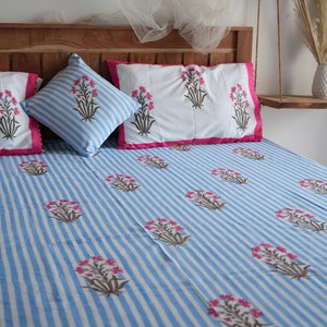 May include: A bed set featuring a blue and white striped pattern with floral accents. The set includes a fitted sheet, pillowcases, and a decorative pillow. The pillowcases have a white background with pink trim. The bed set is made of a soft, comfortable material.