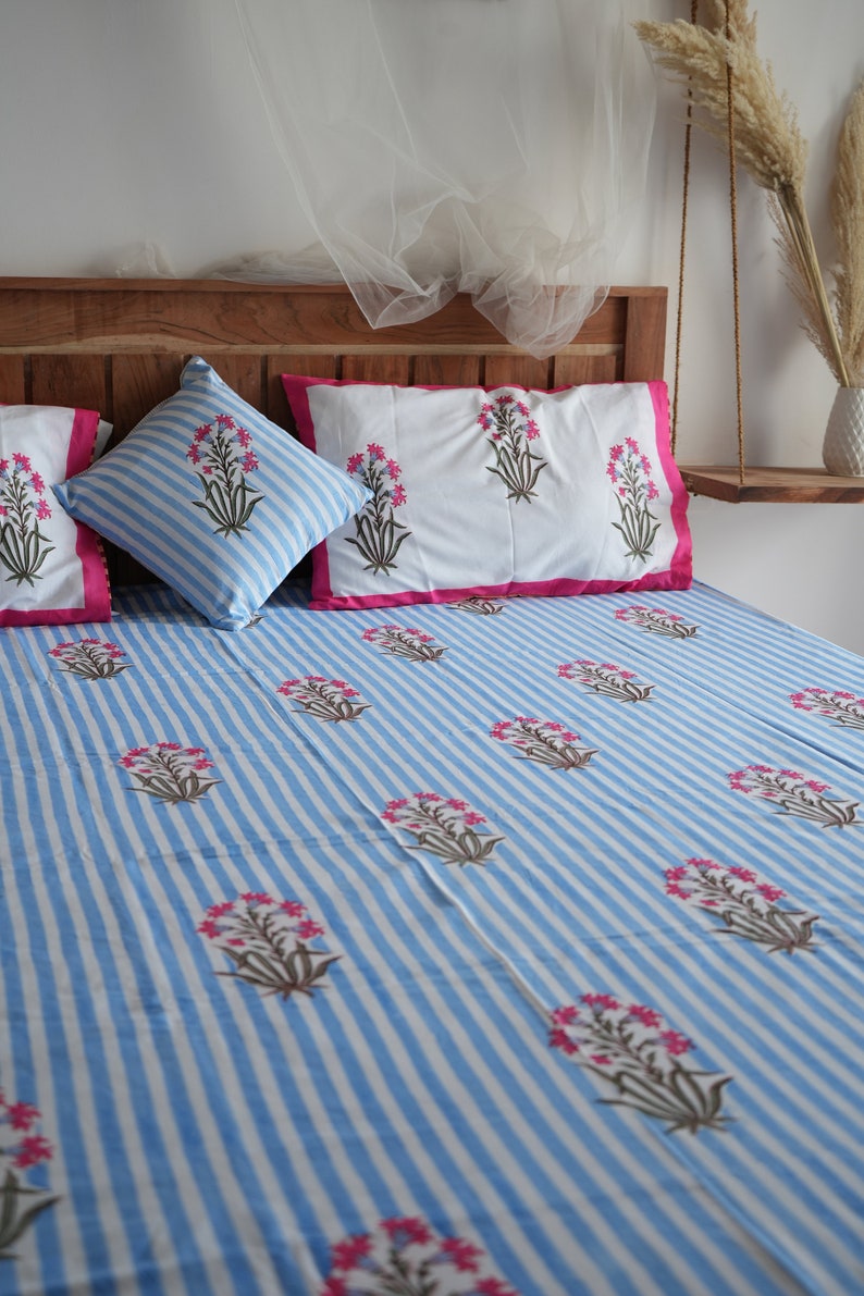 May include: A bed set featuring a blue and white striped pattern with floral accents. The set includes a fitted sheet, pillowcases, and a decorative pillow. The pillowcases have a white background with pink trim. The bed set is made of a soft, comfortable material.