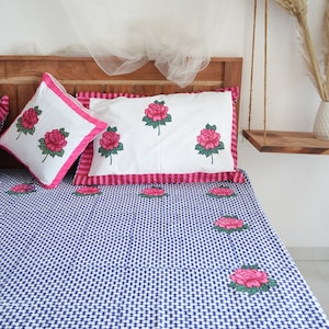 Op de afbeelding: Beddengoedset met bloemenmotief. De set bevat een dekbedovertrek en kussenslopen met een roze rozenpatroon. Het dekbedovertrek heeft een blauw-wit ruitpatroon. De kussenslopen hebben een roze rand.