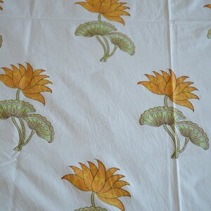 May include: White fabric with a repeating pattern of orange lotus flowers and green leaves. The flowers have multiple petals and are in full bloom. The leaves are a light green color.