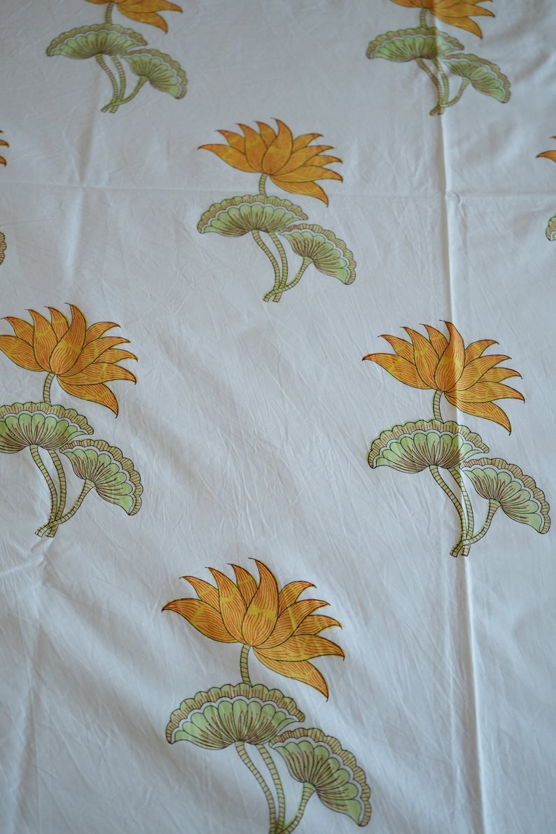 May include: White fabric with a repeating pattern of orange lotus flowers and green leaves. The flowers have multiple petals and are in full bloom. The leaves are a light green color.