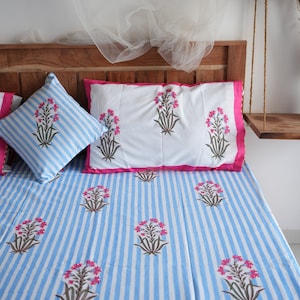 May include: A bed set featuring a blue and white striped pattern. The set includes a fitted sheet, pillowcases, and a decorative pillow, all adorned with floral designs in pink and brown. The pillowcases have a pink border.