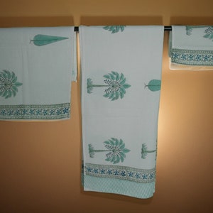 May include: White cotton bedding set with a repeating pattern of stylized palm trees and leaves in shades of teal. The set includes a flat sheet, fitted sheet, and pillowcase, each with a teal border featuring floral and geometric designs.