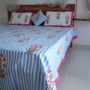 May include: A blue and white striped bedspread with matching pillowcases and a decorative pillow. The bedding features a floral pattern in pink and green. The bedspread has a bright pink border. The bed is made of wood.
