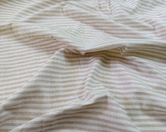 May include: Close-up of a beige and white striped fabric. The fabric is wrinkled, with the stripes running horizontally across the frame. The color palette is neutral, with a mix of light and darker beige tones.