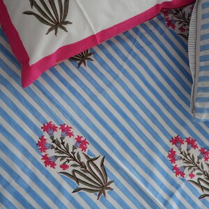 May include: A bedding set featuring a blue and white striped pattern with floral accents. The set includes a white pillowcase with a pink border and a pillowcase with blue and white stripes. The floral design has pink flowers and brown stems.