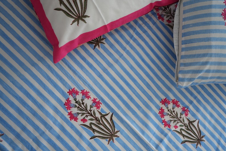 May include: A bedding set featuring a blue and white striped pattern with floral accents. The set includes a white pillowcase with a pink border and a pillowcase with blue and white stripes. The floral design has pink flowers and brown stems.