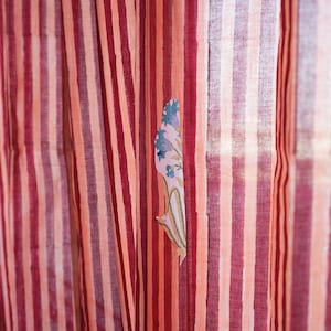 May include: Striped fabric in shades of red and peach, with a floral applique. The vertical stripes alternate between darker and lighter tones, creating a visually appealing pattern. The floral applique adds a delicate touch to the fabric.
