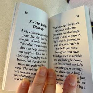 K&ouml;nnte beinhalten: Ein offenes Buch mit Text auf den Seiten, gehalten von einer Hand. Der Text enth&auml;lt den Titel "X - The Bulge Closeup" und andere beschreibende Texte. Das Buch liegt auf einer hellen Oberfl&auml;che.