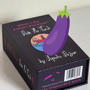 K&ouml;nnte beinhalten: Eine schwarze Schachtel mit "Dick Pic Tarot"-Karten mit dem Text "What's the Future Packing?" und "by Aquata Du jour". Eine lila Aubergine-Grafik ist auf die Schachtel gelegt. Auf der Unterseite der Schachtel steht "The Original Dick Witch."