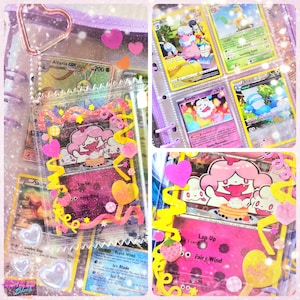 May include: A collection of Pokémon trading cards in a binder and protective sleeves. The cards feature various characters and colorful designs. The binder and sleeves are decorated with pink hearts and yellow embellishments. The cards are in a clear plastic sleeve.
