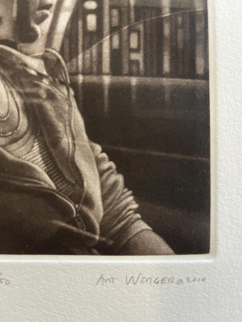 K&ouml;nnte beinhalten: Monochrome Druck einer Person, die einen Kapuzenpullover mit Rei&szlig;verschluss tr&auml;gt. Der Druck ist unten rechts mit "Art Wenger &copy; 2010" signiert. Das Bild ist eine Nahaufnahme, die sich auf den Oberk&ouml;rper und einen Teil des Hintergrunds konzentriert.