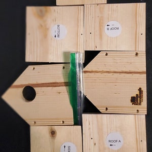 May include: Six pieces of unfinished wood with labels indicating their use in a birdhouse project. The labels include "Roof A", "Roof B", "Side A", "Side B", "Bottom", and "Front".