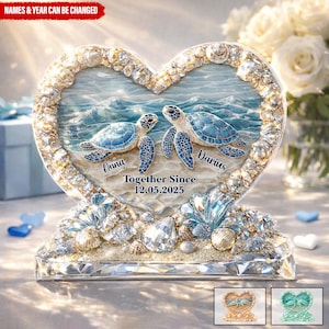 May include: A heart-shaped decorative piece featuring two blue sea turtles on a beach scene. The piece is adorned with crystals, seashells, and the text "Anna" and "Darius" with the date "12.05.2025". The words "Together Since" are also displayed.