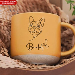 Puede incluir: Taza de cerámica de color amarillo mostaza con un dibujo lineal de un bulldog francés y el nombre "Buddy" en cursiva. La taza tiene una base gris claro y un asa amarilla. El texto "CUSTOM LINE DRAWING FROM YOUR PHOTO" está en la esquina superior izquierda.