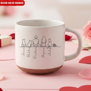 Puede incluir: Taza de cerámica blanca con base y asa marrón. La taza presenta un dibujo lineal negro de una familia con mascotas y los nombres: Josie, Belle, Dieter, Elysia y Judy. El texto "DESIGN CAN BE CHANGED" está en la parte superior.