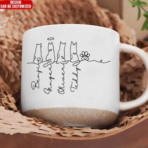 May include: White ceramic mug with a brown base, featuring a black line drawing of four cats and a paw print. The names "Benji", "Ginger", "Oliver", and "Teddy" are written below the cats. The top left corner has the text "DESIGN CAN BE CUSTOMIZED" in a red box.