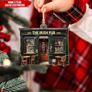 May include: A wooden Christmas ornament shaped like a green pub with the text "EST. THE IRISH PUB 1996" above the door. The pub has two windows, a door, and two barrels in front.