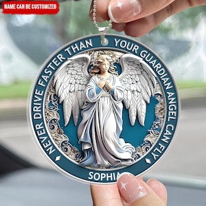 Könnte beinhalten: Ein blauer und weißer Auto-Anhänger mit einem Schutzengel-Motiv. Der Anhänger zeigt einen weißen Engel mit Flügeln, einen blauen Hintergrund und den Text "Fahre niemals schneller als dein Schutzengel fliegen kann". Der Name "Sophia" ist am unteren Rand des Anhängers aufgedruckt.