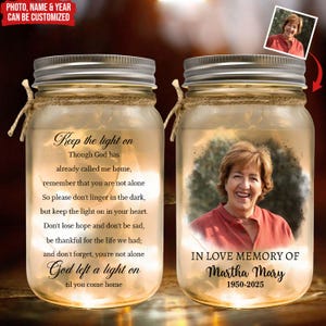 May include: Two glass mason jars with silver lids and twine. One jar displays a photo and the text "IN LOVE MEMORY OF Martha Mary 1950-2025." The other jar has a poem that starts "Keep the light on." The jars are customisable.