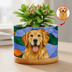 May include: A ceramic plant pot featuring a Golden Retriever design with a stained-glass effect. The pot has a bamboo base and is filled with a green plant with small pink flowers. A smaller image of the dog is shown on the right.