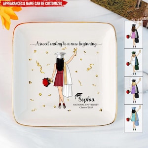 May include: A white ceramic trinket tray with a gold rim. The tray features a graduation cap, a woman in a red dress and a white gown, and gold confetti. The text "A sweet ending to a new beginning" and "Sophia National University Class of 2025" is printed on the tray.