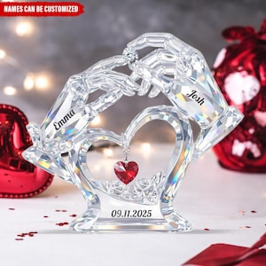 May include: A clear crystal ornament depicting two hands presenting a diamond ring above a heart-shaped design. The names "Emma" and "Josh" are engraved on the hands, with the date "09.11.2025" at the base. The text "NAMES CAN BE CUSTOMIZED" is at the top.