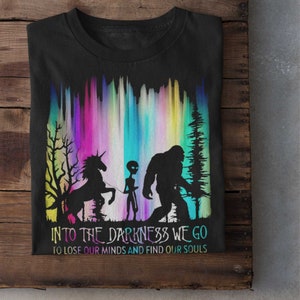 May include: Black t-shirt with a graphic of a unicorn, alien, and Bigfoot walking into a colorful aurora borealis. The text reads "Into the darkness we go to lose our minds and find our souls."