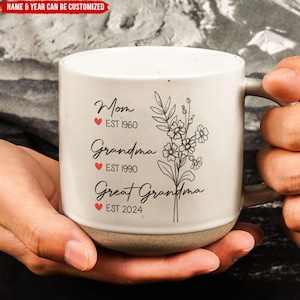 Puede incluir: Taza de cerámica blanca con texto negro y un diseño floral. El texto dice "Mom EST 1960 Grandma EST 1990 Great Grandma EST 2024".