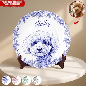 May include: A white decorative plate with a blue floral border and a detailed illustration of a dog. The dog's name, "Bailey," is written in cursive. The plate is displayed on a brown stand.