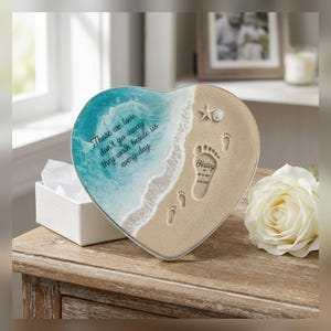 May include: A heart-shaped plaque featuring a beach scene with turquoise ocean waves, sandy shore, a starfish, and footprints. The text reads: Those we love don't go away they walk beside us every day. A footprint includes the name Hailey.