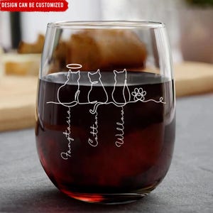 May include: A stemless wine glass filled with red liquid. The glass features a white line drawing of three cats and a paw print. The names "Fangtasia", "Cotton", and "Willow" are written below the cats. The text "DESIGN CAN BE CUSTOMIZED" is in a red banner.