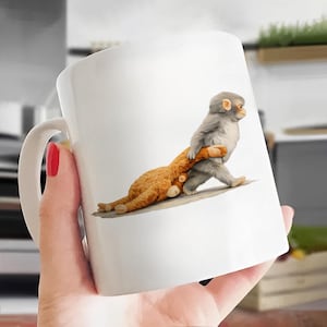 May include: White ceramic mug featuring a whimsical illustration of a gray monkey carrying a brown teddy bear. The monkey is walking, and the bear is lying down. The mug has a white handle and is held by a person.