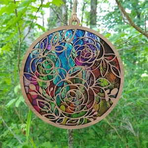 May include: A round wooden ornament featuring a colourful floral design. The ornament is cut out in a delicate pattern, revealing the colourful background. The ornament is ideal for adding a touch of nature to your home decor.