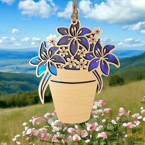 Puede incluir: Adorno de maceta de madera con un diseño floral azul y morado. La maceta está colgada de una cuerda y tiene un aspecto rústico y hecho a mano.
