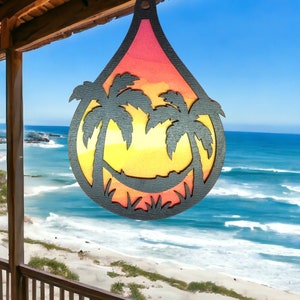 May include: A wooden cutout of a sunset with palm trees, hanging in front of a beach scene with blue water and white sand.
