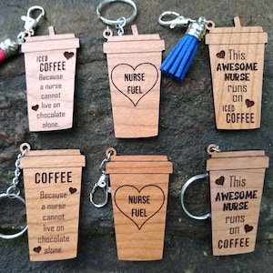 May include: Six wooden coffee cup keychains with different sayings. The keychains are brown and feature a white design. The sayings include "Iced Coffee Because a Nurse Cannot Live on Chocolate Alone", "Nurse Fuel", "This Awesome Nurse Runs on Iced Coffee", and "Coffee Because a Nurse Cannot Live on Chocolate Alone".