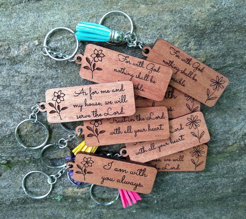 May include: A set of wooden keychains with inspirational quotes and floral designs. The keychains are engraved with phrases like "For with God nothing shall be impossible" and "As for me and my house, we will serve the Lord."