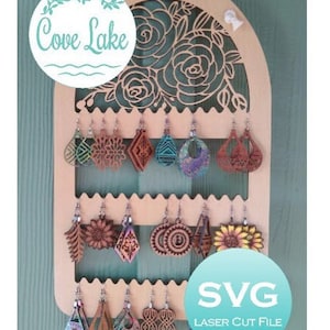 May include: Wooden earring holder with a floral design and a scalloped edge. The holder has three rows of hooks for earrings. The holder is labelled "SVG Laser Cut File".