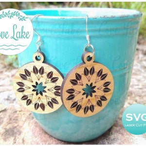 May include: A pair of wooden earrings with a laser-cut mandala design. The earrings are brown and have a light wood color. The mandala design features a star in the center and leaves around the star. The earrings are hanging from silver hooks.