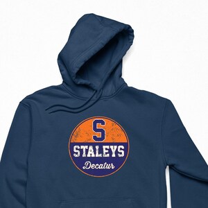 May include: A navy blue hooded sweatshirt with a vintage-style circular logo featuring an orange background, a white "S" and the text "Staleys Decatur" in white.