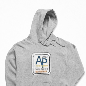 Puede incluir: Sudadera con capucha gris con un logotipo de estilo vintage que presenta las letras "AP" en azul y amarillo, con el texto "Green Bay, WI 1921 FOOTBALL" debajo.