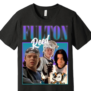 Puede incluir: Camiseta negra con un gráfico de tres personas y el texto "Fulton Reed" en una fuente retro. El gráfico utiliza colores turquesa y morado, y las personas llevan equipo de hockey y una bandana.