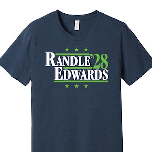 May include: A navy blue t-shirt with a white graphic that says "Randle'28 Edwards" in green letters with stars above and below the text.