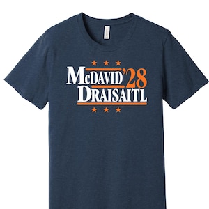 May include: A navy blue t-shirt with a white and orange graphic that says "McDavid'28 Draisaitl" with five stars above and below the text.