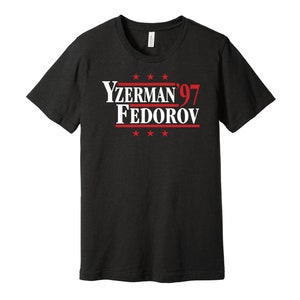 May include: Black t-shirt with white text that reads "Yzerman'97 Fedorov" in a political campaign style font. There are five red stars above and below the text.