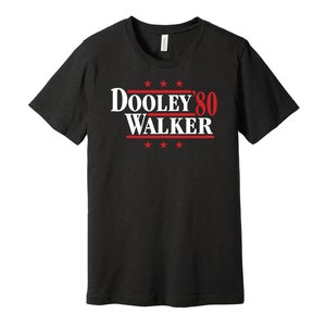 Puede incluir: Camiseta negra con un gráfico blanco que dice "Dooley '80 Walker" en texto rojo y blanco. Hay cinco estrellas rojas encima del texto y cinco estrellas rojas debajo del texto.