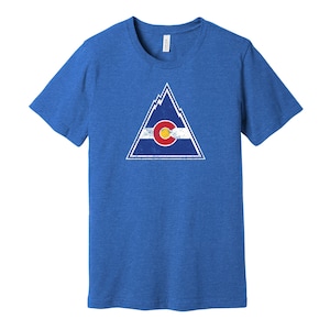 Puede incluir: Una camiseta azul real con un gráfico de triángulo blanco desgastado que presenta la bandera del estado de Colorado. La bandera es azul, blanca y roja con un gran círculo amarillo en el centro.