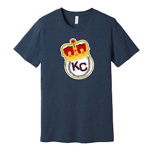 May include: A navy blue t-shirt with a distressed graphic of a baseball with a crown on top and the letters "KC" inside.